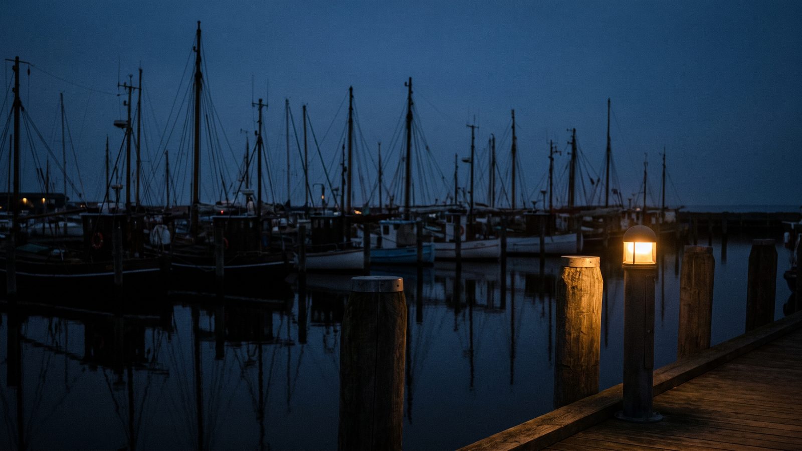 Fiskerbåde og master i blå time, en lanterne tændt på broen