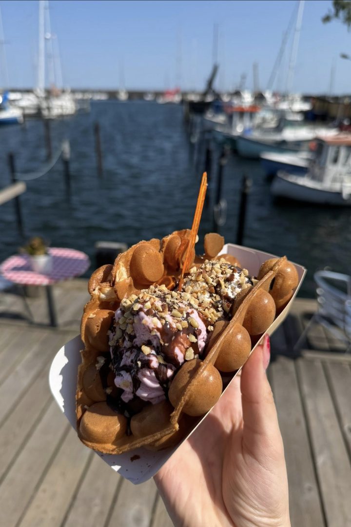 En bubblewaffle med is, chokolade og hakkede nødder holdt op foran havnen